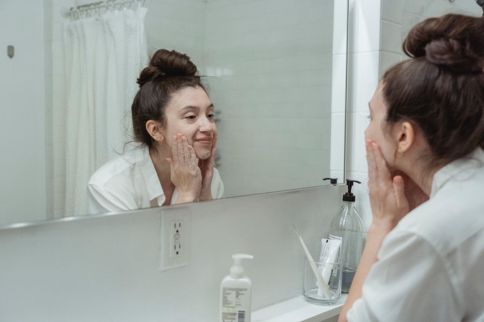Jeune femme appliquant une crème hydratante devant un miroir de salle de bain